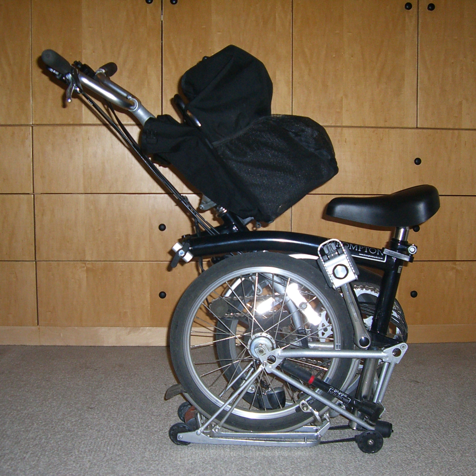 Black Brompton folding bike, half folded, with front bag